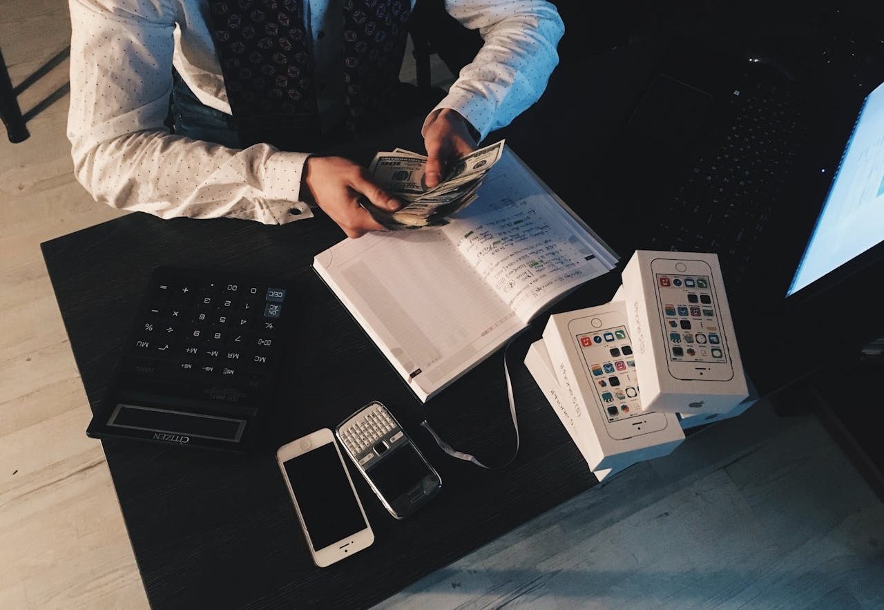 Businessman organizing finances with tech devices and cash on desk.